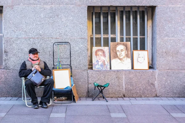 Retratista callejero con ejemplos de su trabajo a la espera de los turistas su cerca de la Plaza del Palacio en San Petersburgo, Rusia — Foto de Stock