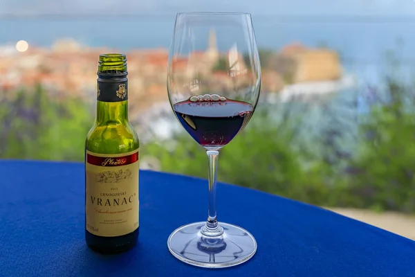 Sklenice a malá láhev červeného vína s Budva starým městem a Jaderským mořem v Černé hoře v pozadí — Stock fotografie