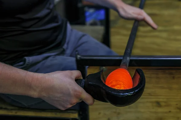 Glass blower shaping a bubble of melted glass on a rod by hand at a glass maker's workshop, shallow depth of field