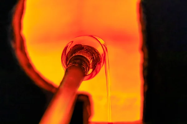 Soffiatore di vetro che lavora su una bolla di vetro fuso su un'asta riscaldandola in un forno presso un'officina di produzione di vetro — Foto Stock