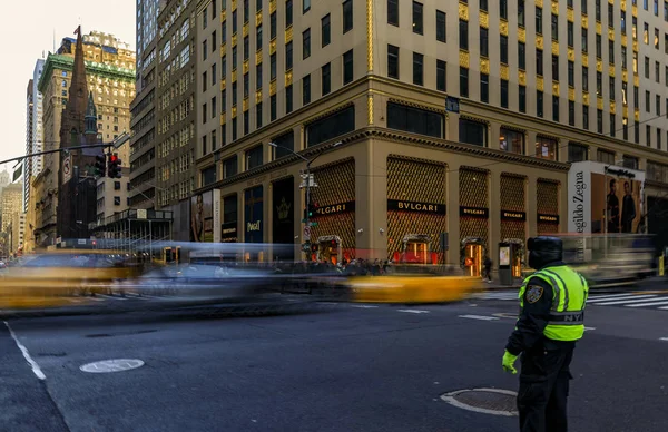 Verschwommene gelbe Taxis rasen an Menschen und Verkehrspolizisten an einer belebten Kreuzung auf der 5th Avenue in Manhattan, New York, USA vorbei. — Stockfoto