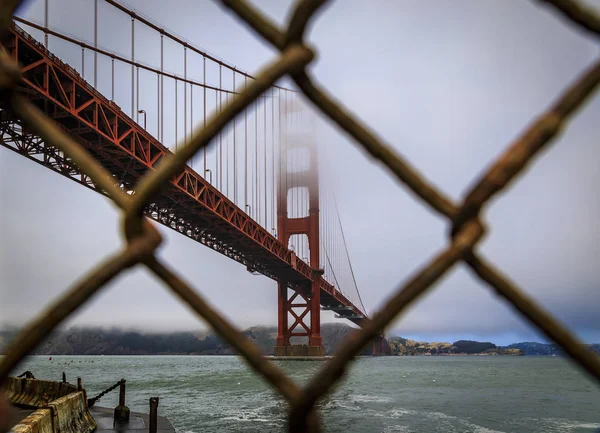 A famosa ponte Golden Gate vista através de uma cerca ferrugenta em um dia nublado em São Francisco, Califórnia — Fotografia de Stock