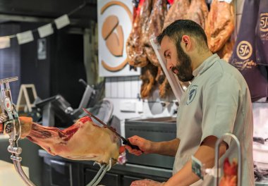 Madrid, İspanya 'da yerel bir markette müşteriler için tezgahta koca bir Serrano Iberico jambonu dilimliyor.