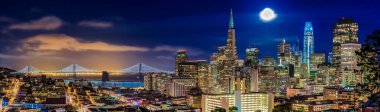 Gün batımında San Francisco şehrinin gökyüzü manzarası. Gökdelenler arasında gökyüzü çizgisi, Bay Bridge ve Ina Serin Doğum Parkı 'ndan izlenen dolunay var.