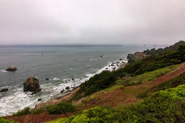 ABD 'nin San Francisco kentindeki Lands End patikasından görülen sisle kaplı engebeli sahil kayalıklarına ve Golden Gate Köprüsü' ne bakın.