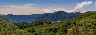 Karadağ 'ın Novoselje kenti yakınlarındaki engebeli dağların panoramik manzarası, alçak asılı bulutlar ve kırmızı terakotta fayanslı çatıları olan küçük bir yerleşim yeri