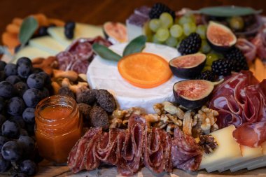 Pişmiş et, jambon, salam ve kopa, peynir, çedar peyniri ve adaçayı ile süslenmiş diğer peynirler ve meyvelerle dolu yiyecek kurulu.