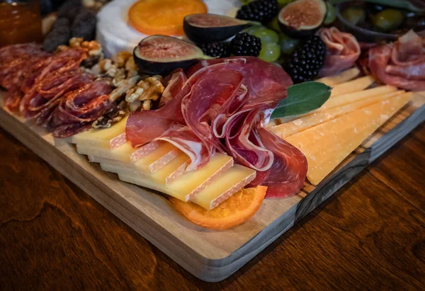 Placa de alimentos com carnes curadas prosciutto, salame e coppa, brie, cheddar e outros queijos e frutas decorados com sálvia — Fotografia de Stock