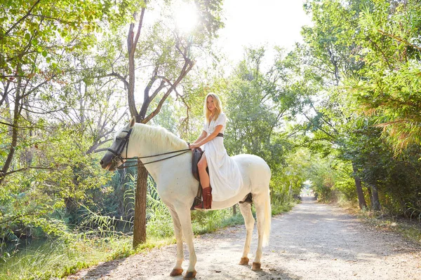 一个金发女郎骑着白色的马在森林的跑道上户外 — 图库照片