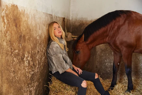 ストローベイルの茶色の馬と屋内の安定に金髪の女性 — ストック写真