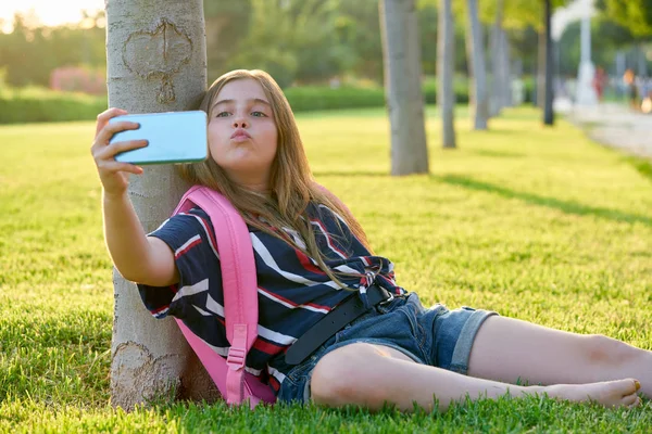 学校に戻って公園でスマート フォンで金髪の学生の子供女の子が草の上に座る — ストック写真