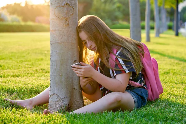 学校に戻って公園でスマート フォンで金髪の学生の子供女の子が草の上に座る — ストック写真