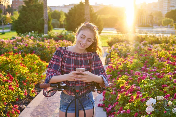 青少年女孩自行车玩智能手机在城市花卉公园 — 图库照片