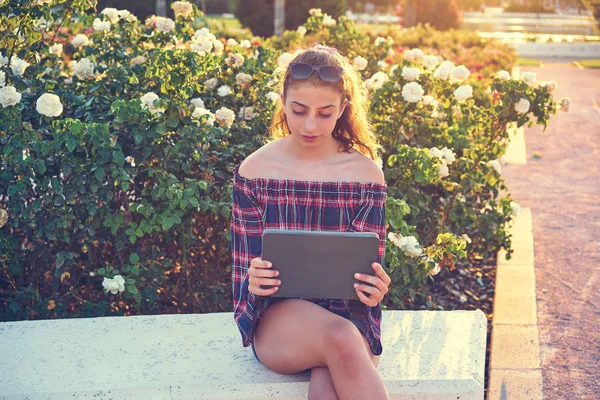 Κορίτσι Που Κάθεται Παγκάκι Που Παίζει Tablet Φόντο Ροδαλά Λουλούδια — Φωτογραφία Αρχείου