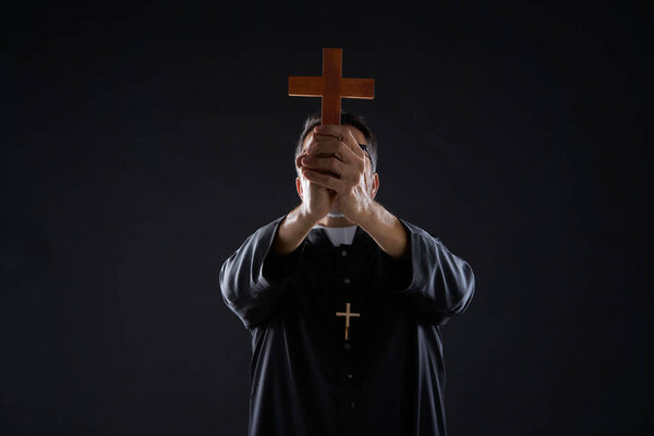 Priest holding cross of wood praying in foreground