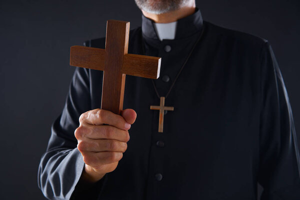 Priest holding cross of wood praying in foreground