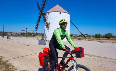 Biker pilgrim by Camino de Santiago in bicycle at windmill of Castile La Mancha clipart