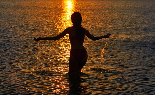 オレンジ色の空に夕日のビーチで手で水しぶきの女の子 — ストック写真