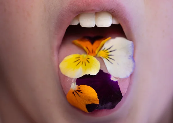 Девушка ест съедобные лепестки цветов во рту — стоковое фото