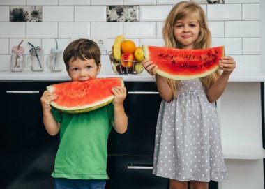 Mutfakta karpuz yiyen mutlu gülümseyen üç çocuk. Yaz sağlıklı yiyecekler.