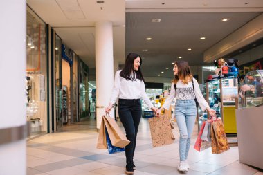 Güzel genç anne ve genç kızı alışveriş merkezinde alışveriş yaparken alışveriş çantaları tutuyor ve gülümsüyor. Aile alışverişi.