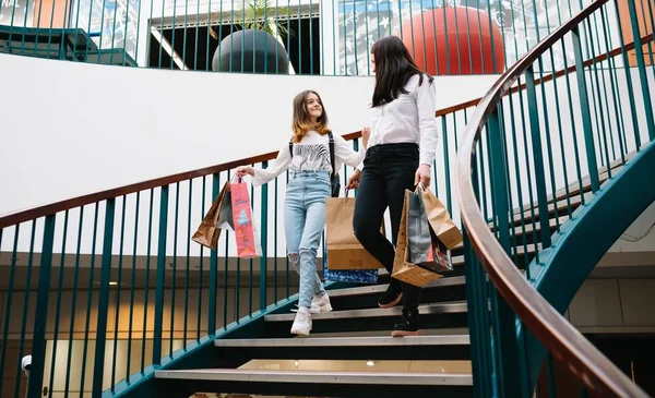 Hermosa mamá joven y la hija adolescente están sosteniendo bolsas de compras y sonriendo mientras hacen compras en el centro comercial. Compras familiares . —  Fotos de Stock
