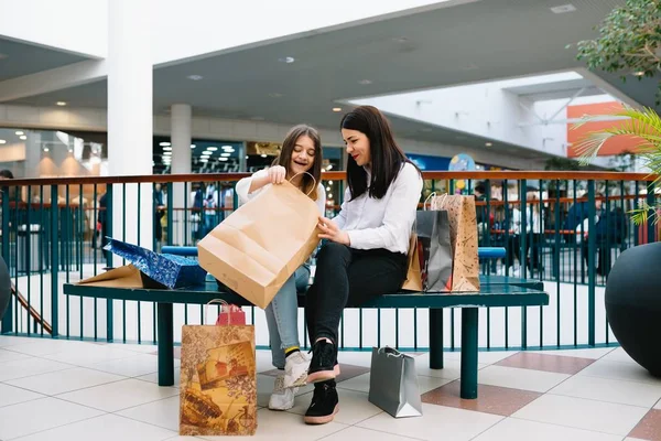 美しい若いママと十代の娘は、ショッピングモールで買い物をしながら、買い物袋を保持し、笑顔です。ファミリーショッピング. — ストック写真