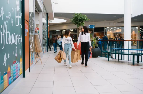 Hermosa mamá joven y la hija adolescente están sosteniendo bolsas de compras y sonriendo mientras hacen compras en el centro comercial. Compras familiares . —  Fotos de Stock