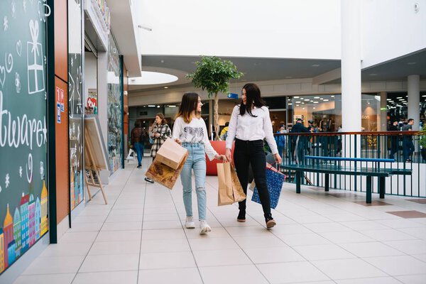 Beautiful young mom and teenage daughter are holding shopping bags and smiling while doing shopping in mall. Family shopping.