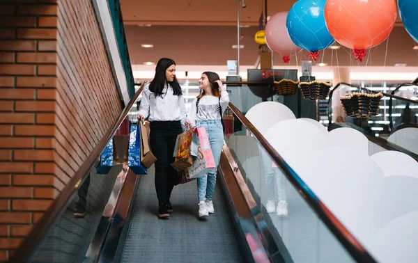 Güzel genç anne ve genç kızı alışveriş merkezinde alışveriş yaparken alışveriş çantaları tutuyor ve gülümsüyor. Aile alışverişi. — Stok fotoğraf