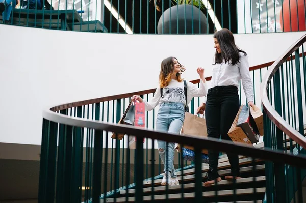 Beautiful young mom and teenage daughter are holding shopping bags and smiling while doing shopping in mall. Family shopping.