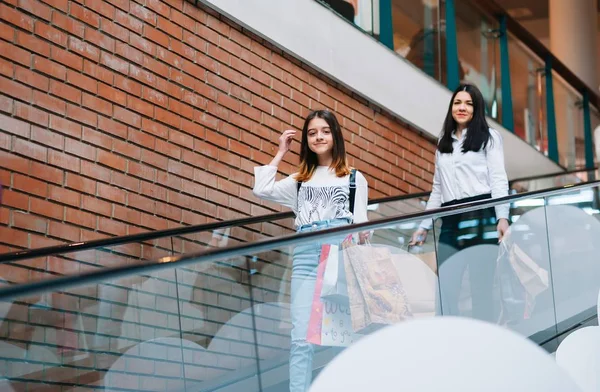 Schöne junge Mutter und Teenager-Tochter halten Einkaufstüten in der Hand und lächeln, während sie im Einkaufszentrum einkaufen. Familieneinkauf. — Stockfoto