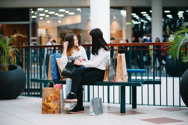 Bela jovem mãe e filha adolescente estão segurando sacos de compras e sorrindo ao fazer compras no shopping. Compras familiares . — Fotografia de Stock