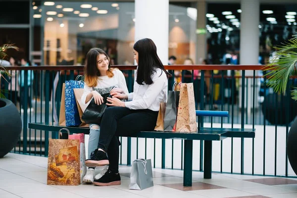 Bela jovem mãe e filha adolescente estão segurando sacos de compras, fazendo compras no shopping. Compras familiares . — Fotografia de Stock