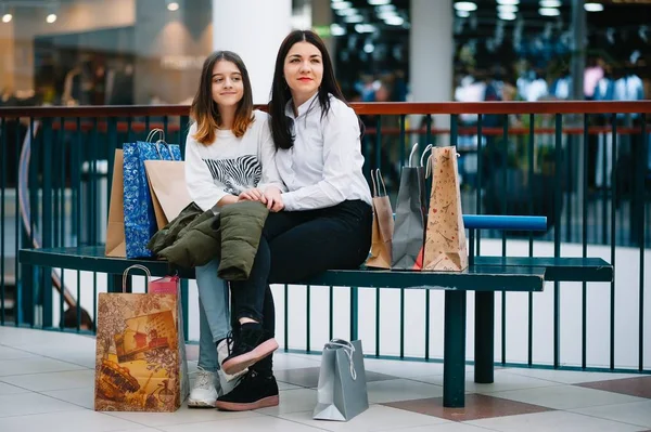 Beautiful young mom and teenage daughter are holding shopping bags, shopping in mall. Family shopping.