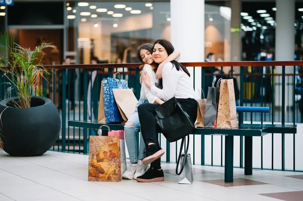 Bela jovem mãe e filha adolescente estão segurando sacos de compras, fazendo compras no shopping. Compras familiares . — Fotografia de Stock