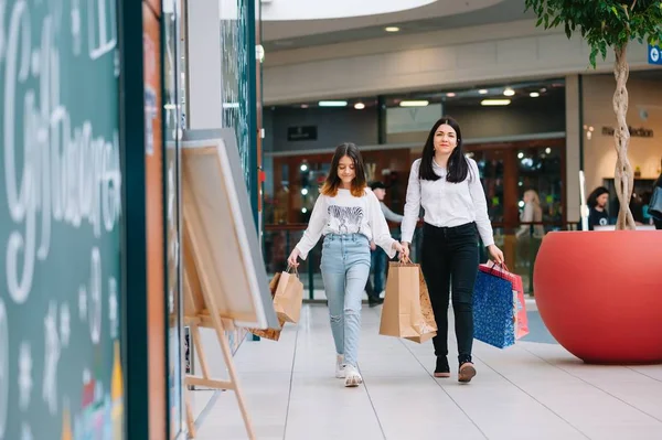 Bela jovem mãe e filha adolescente estão segurando sacos de compras e sorrindo ao fazer compras no shopping. Compras familiares . — Fotografia de Stock