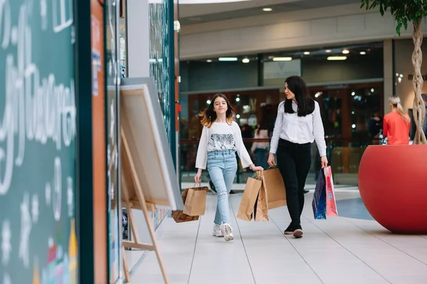 Gyönyörű fiatal anya és tizenéves lánya gazdaság bevásárló táskák és mosolygott, miközben vásárol a plázában. Családi vásárlás. — Stock Fotó