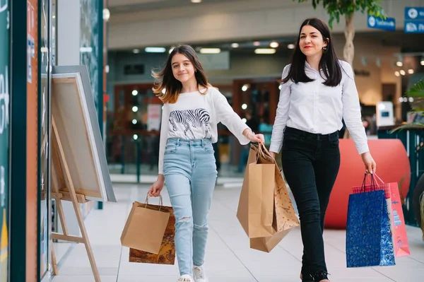 Bela jovem mãe e filha adolescente estão segurando sacos de compras e sorrindo ao fazer compras no shopping. Compras familiares . — Fotografia de Stock