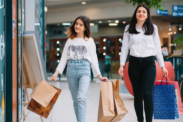 Beautiful young mom and teenage daughter are holding shopping bags, shopping in mall. Family shopping.