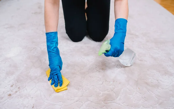 People, housework and housekeeping concept - close up of woman in rubber gloves with cloth and derergent spray cleaning carpet at home. close up of woman with cloth cleaning carpet — Stock Photo, Image