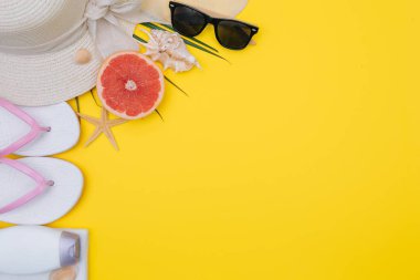 Düz yatıyordu plaj aksesuarları: mayo, güneş gözlüğü, şapka, palmiye dalları ile sandalet, egzotik meyve ve kabukları. Sarı arka planda üstte görünüm