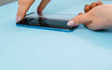 Ekranlı akıllı telefon elinde cam kapağı korur. mavi arka plan. kadın el sopa temperli cam kalkan veya cep telefonu ile film ekran kapağı. koruyucu kavramlar fikirler