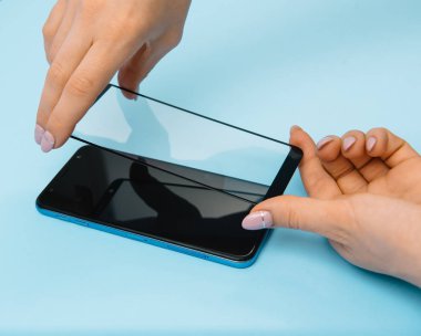 Ekranlı akıllı telefon elinde cam kapağı korur. mavi arka plan. kadın el sopa temperli cam kalkan veya cep telefonu ile film ekran kapağı. koruyucu kavramlar fikirler