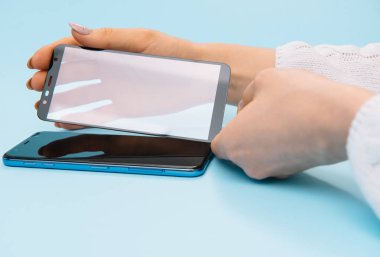 Ekranlı akıllı telefon elinde cam kapağı korur. mavi arka plan. kadın el sopa temperli cam kalkan veya cep telefonu ile film ekran kapağı. koruyucu kavramlar fikirler