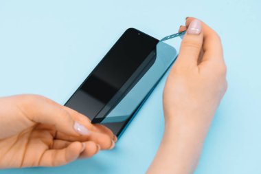 Ekranlı akıllı telefon elinde cam kapağı korur. mavi arka plan. kadın el sopa temperli cam kalkan veya cep telefonu ile film ekran kapağı. koruyucu kavramlar fikirler