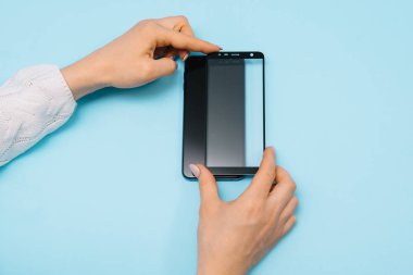 Ekranlı akıllı telefon elinde cam kapağı korur. mavi arka plan. kadın el sopa temperli cam kalkan veya cep telefonu ile film ekran kapağı. koruyucu kavramlar fikirler