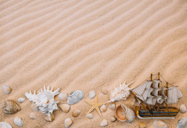Snäckskal och segelfartyg med sand som bakgrund. Sommar strand. Översta vyn. Bakgrund med kopierings utrymme och synlig sand textur — Stockfoto