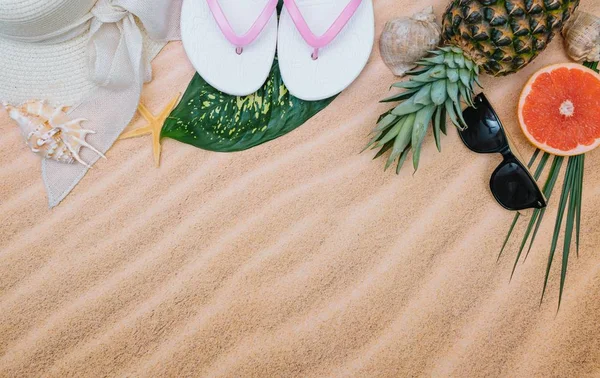 Bovenaanzicht van zandstrand met handdoek frame en zomer accessoires: zonnehoed, handdoek, badpak, slippers, zonnebrandcrème fles, exotische vruchten, en schelpen. Achtergrond met Kopieer ruimte en zichtbare zand textuur. — Stockfoto