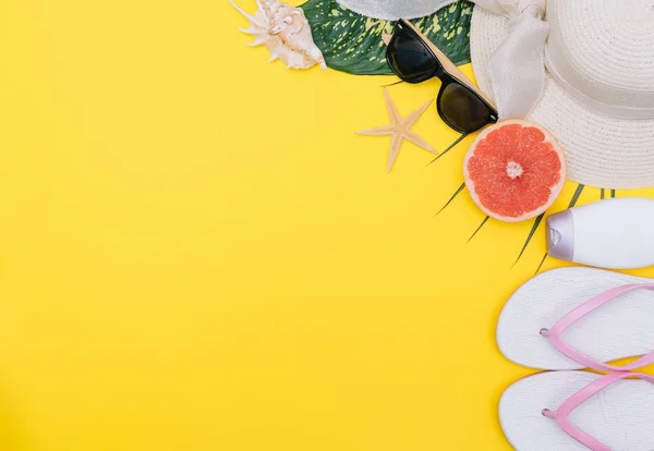 Beach flat lay accessories. Sun hat, towel, camera, cream, swimsuit, slippers, sunscreen bottle, exotic fruits, and seashells on a yellow background. Summer travel holiday concept